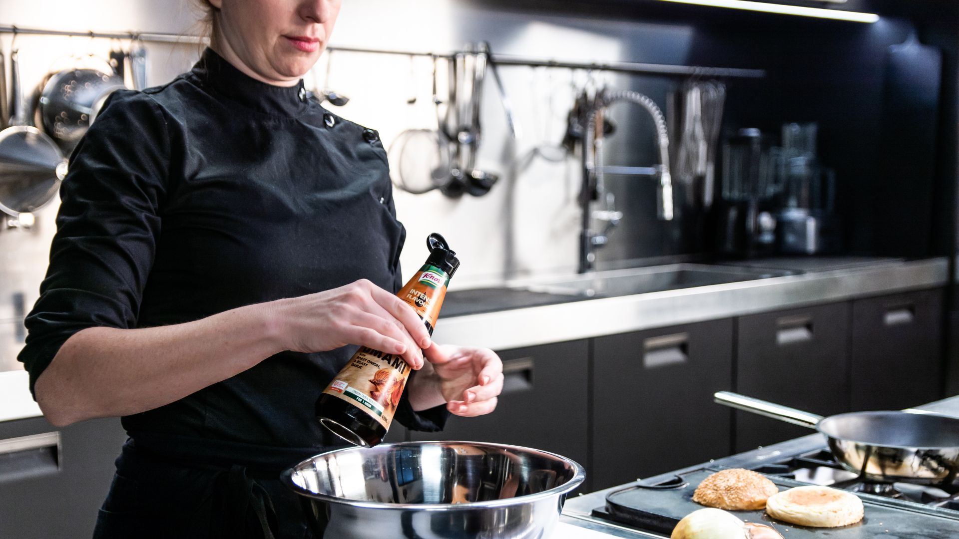 Vrouwelijke chef-kok in professionele keuken die een flesje Knorr Intense Flavours in een kom mengt.