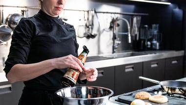 Vrouwelijke chef-kok in professionele keuken die een flesje Knorr Intense Flavours in een kom mengt.