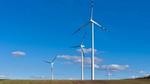 Een rij windturbines staat in een omgeploegd veld, tegen een helderblauwe lucht