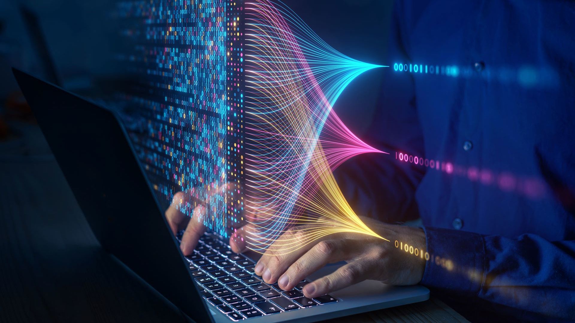Een zilverkleurige laptop met zwarte toetsen, handen op een toetsenbord, met daaroverheen een keur aan kleurrijke digitale code die naar technologie verwijst.