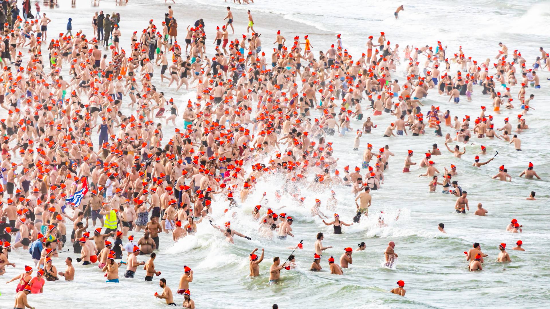 Een grote groep mensen, velen met feloranje hoeden, waadt door de oceaan.