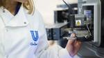 Een close-upfoto van een wetenschapper in een witte laboratoriumjas van Unilever, die door een grote digitale microscoop kijkt.