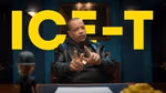 Persoon die aan een bureau zit en met beide handen gebaart, met grote gele tekst "ICE-T" op de achtergrond.