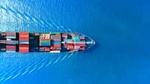 Een afbeelding van een boot van bovenaf, geladen met zeecontainers, varend op open water.