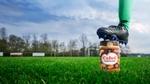 Een voet met een voetbalschoen rust op een pot Calvé pindakaas op een grasveld.