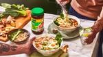 Een tafel gedekt met twee kommen met ramennoedels, een snijplank met ingrediënten en een pot met Knorr-kippenbouillon.